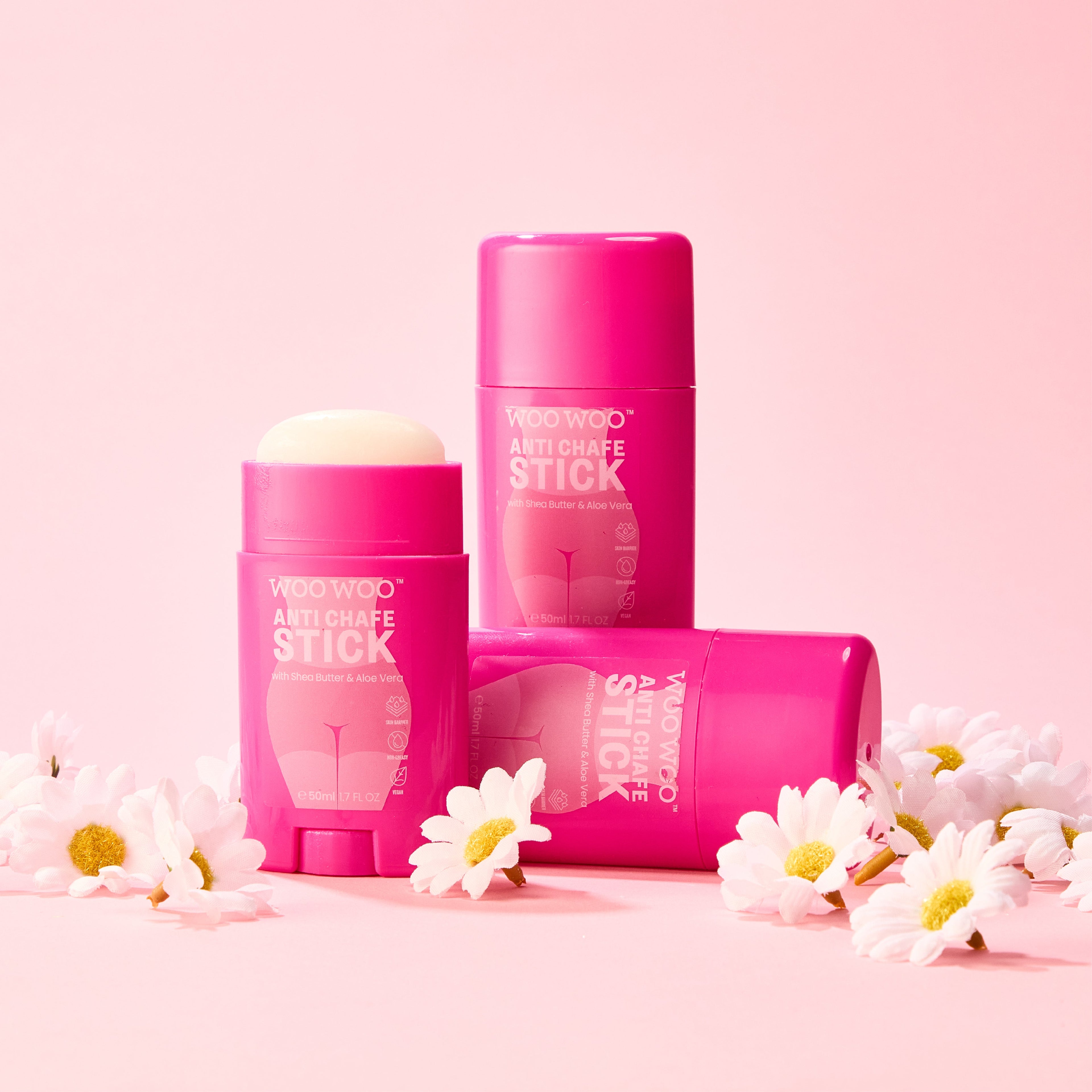 Multiple WooWoo anti chafe sticks surrounded by daises and a pink background