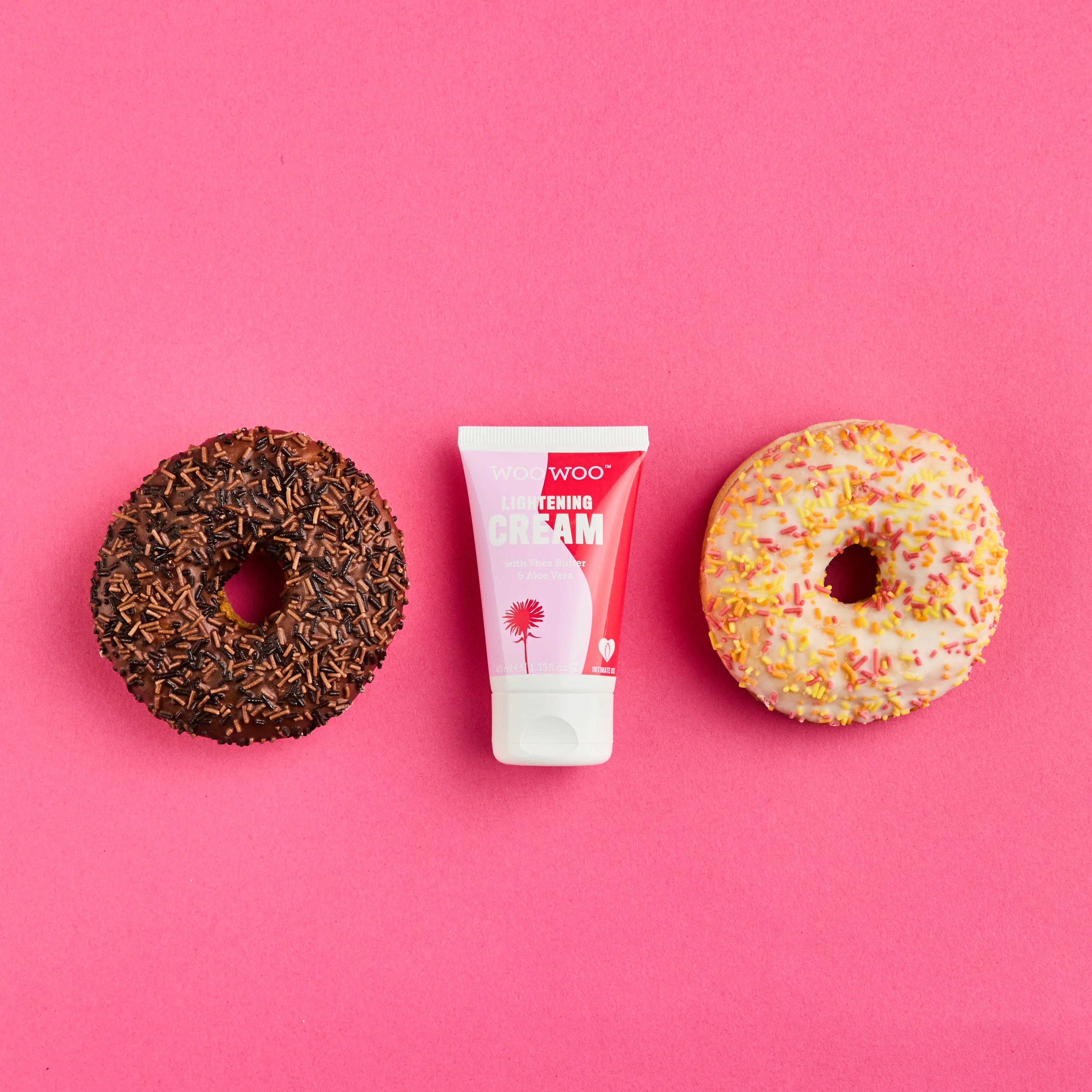 Two donuts and a tube of cream on a pink background
