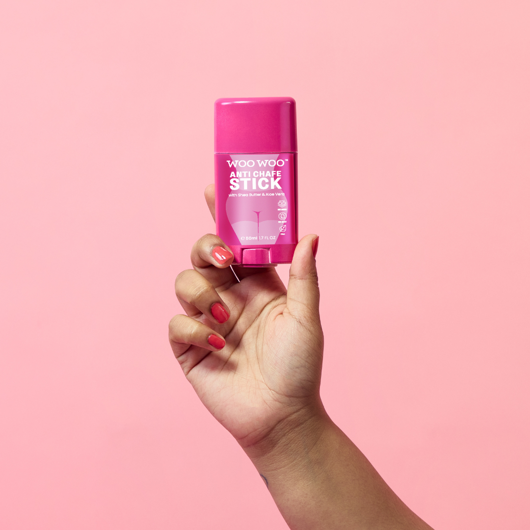 WooWoo anti chafe stick being held in the air on a pink background