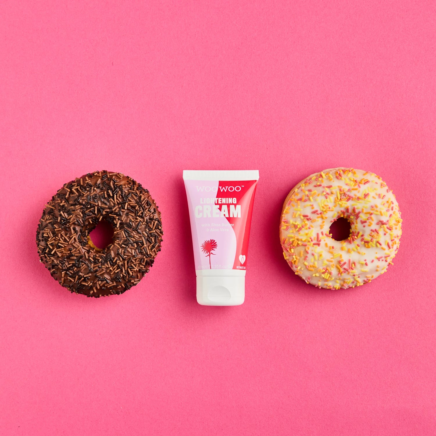 Two donuts and a tube of cream on a pink background