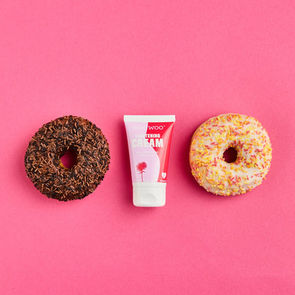 Two donuts and a tube of cream on a pink background