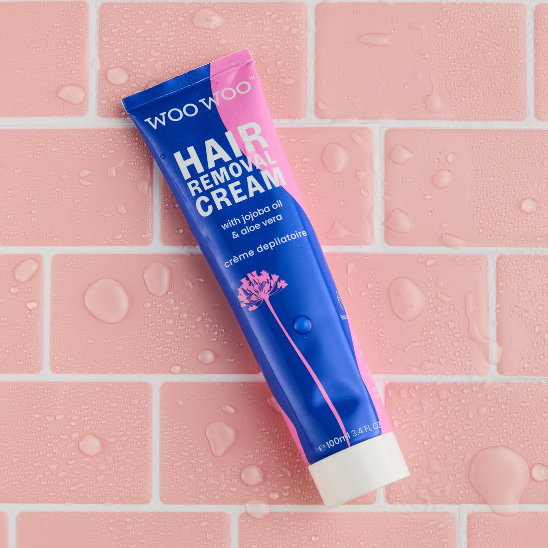 Tube of WooWoo hair removal cream on pink brick background with water spots